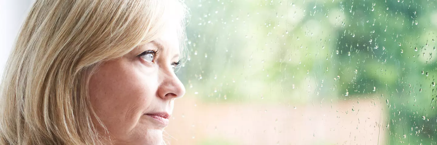 Frau schaut durch verregnetes Fenster