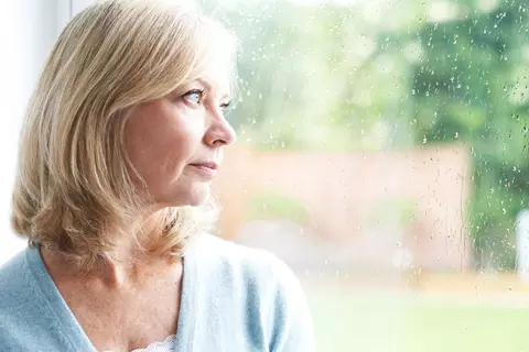 Frau schaut durch verregnetes Fenster